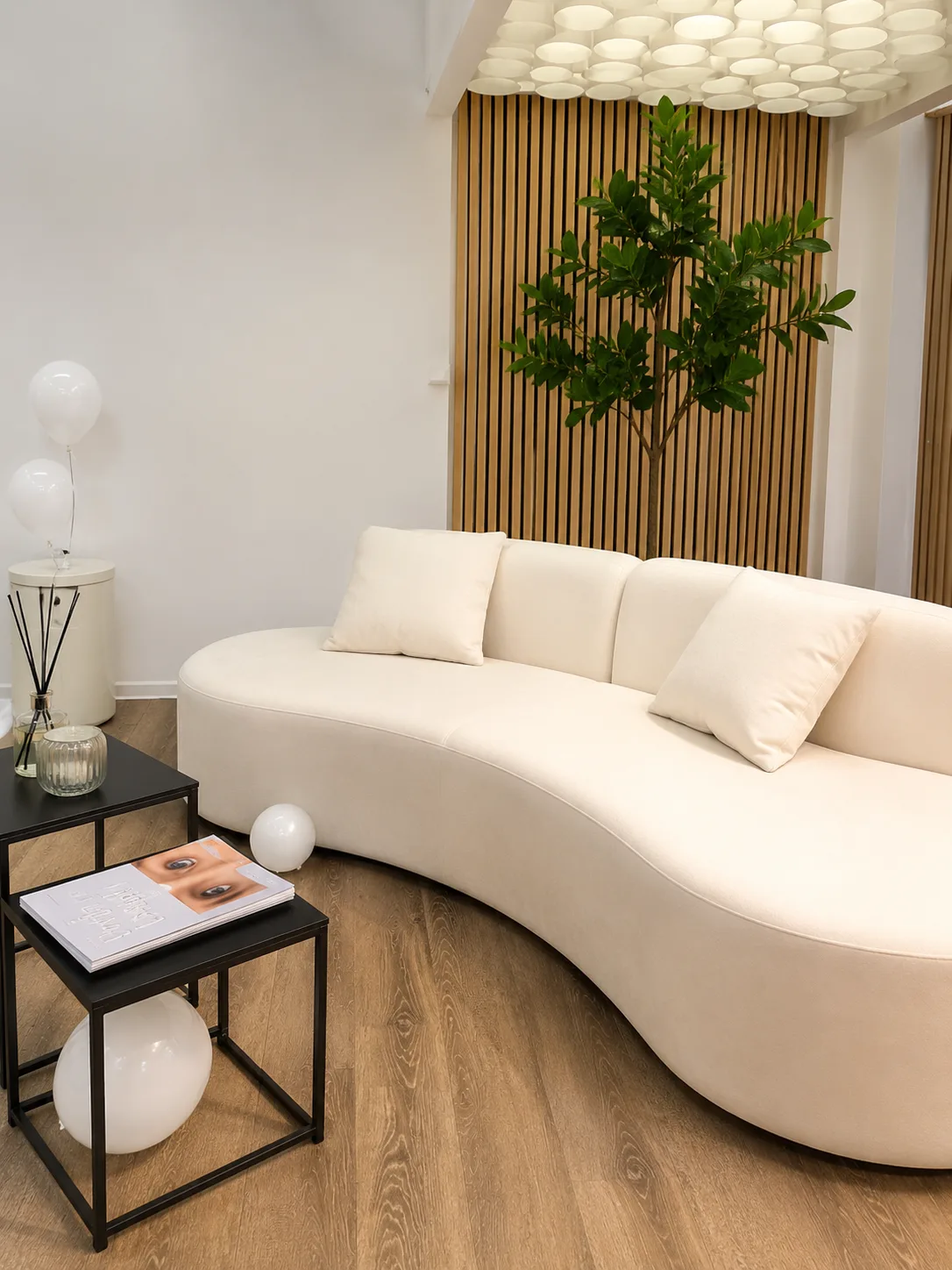 Lounge-Bereich im Lessa Aesthetics Studio mit geschwungenem Bouclé-Sofa und Eichenholz-Lamellen